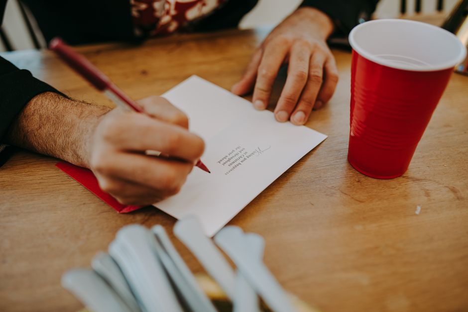 Close-up of hands writing a letter at a cozy home setting with a red solo cup and utensils.